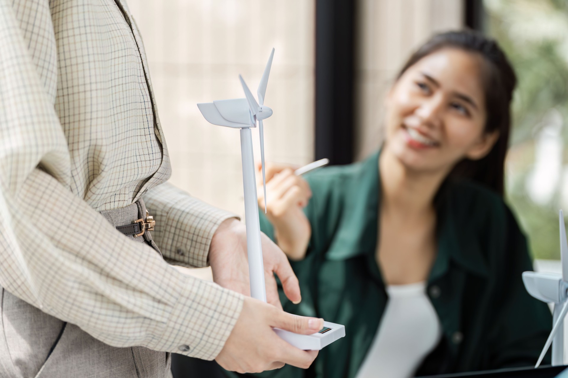Renewable Energy and Teamwork. A professional presenting a model wind turbine during a strategic meeting.